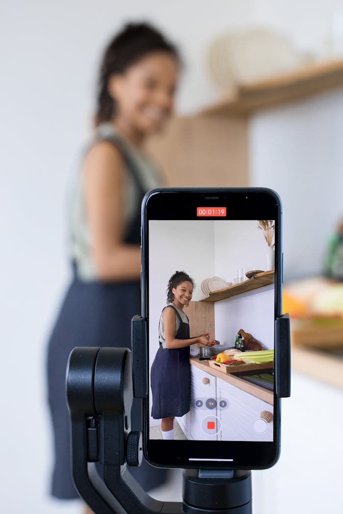 Woman vlogging her cooking tutorial in a kitchen using smartphone on a tripod.